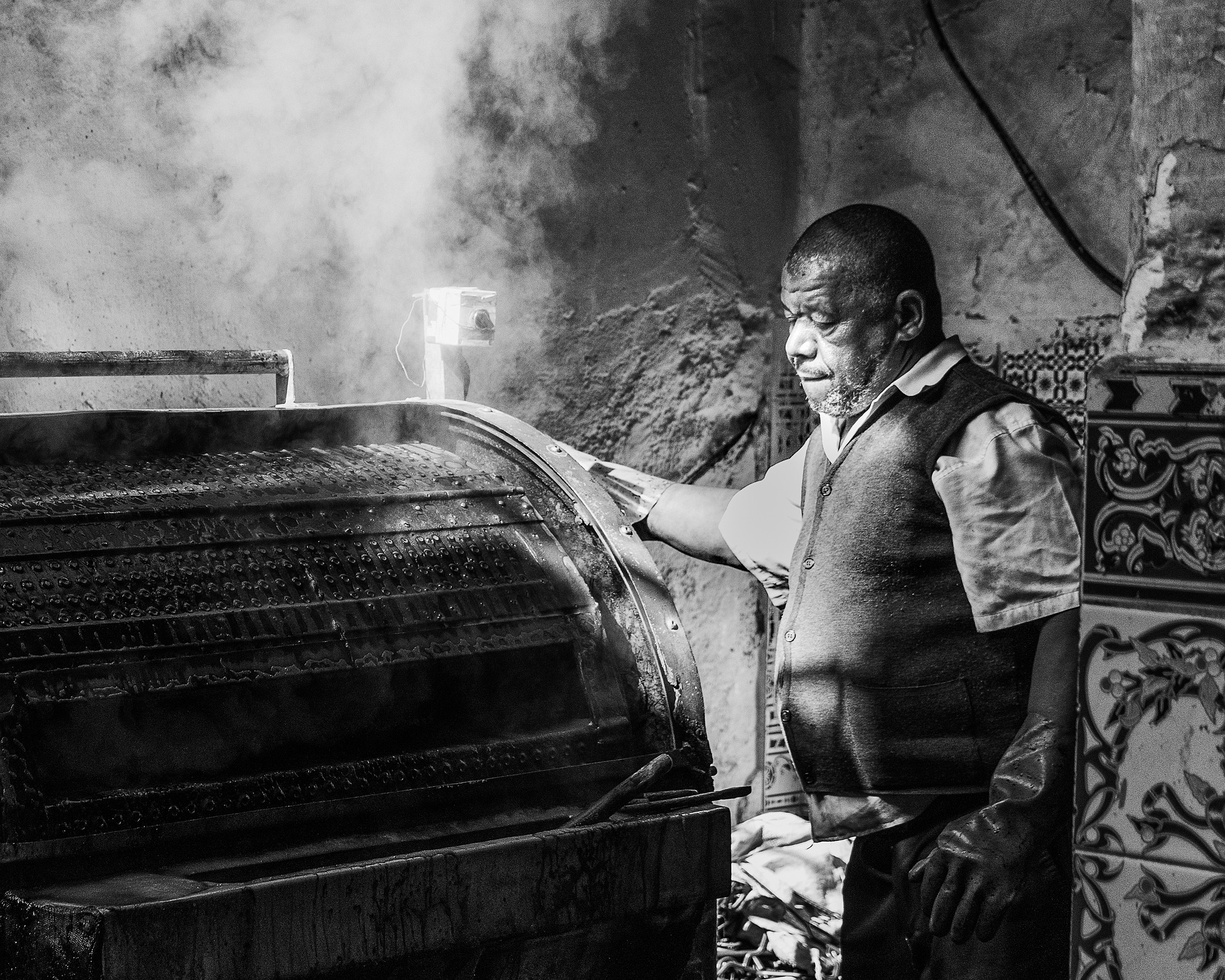 Geschichte der Gerberei: Ein Gerber bei der Arbeit an einer dampfenden altertümlichen Ledertrommel vor Jahrzehnten. Blick in eine historische Gerberei: Ein erfahrener Gerber an einer dampfenden altertümlichen Ledertrommel.